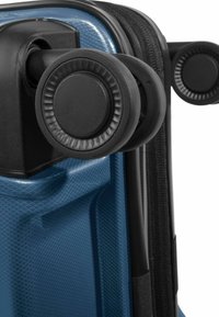 Quatre roues pivotantes noires attachées à l'angle d'une valise rigide bleue texturée avec une fermeture éclair noire.