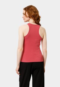 Top de tirantes rojo con diseño de espalda nadadora, que presenta una silueta ajustada y tejido suave, combinado con pantalones negros de corte holgado.