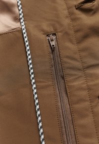 Rjavo sintetično blago z detajlom zadrge. Črno-beli karo poudarki ob strani zadrge. Gladek tekstura z rahlo sijočim zaključkom.