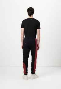 Zwarte t-shirt met Hugo-logo, gecombineerd met zwarte joggers met een rood zijpaneel en elastische tailleband, afgewerkt met witte sneakers.