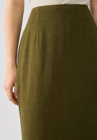 Olive green linen skirt with a smooth texture, high waist, and subtle pleats. The fabric has a slightly textured finish.