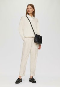 Crème kleurige trui, witte blouse met kraag, lichtbeige broek, zwarte leren schoudertas en zwarte patent leren schoenen met een platte zool.