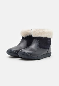 Botă din piele neagră cu o parte din suede bleumarin, având un manșon din blană sintetică crem pufoasă și un talpă din cauciuc texturat pentru aderență.