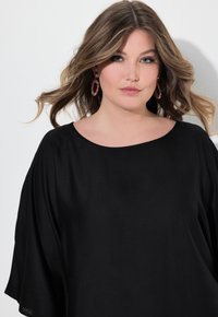 Top nero a maniche a pipistrello con scollatura ampia, texture liscia e maniche corte, abbinato a orecchini a cerchio floreali rosa.