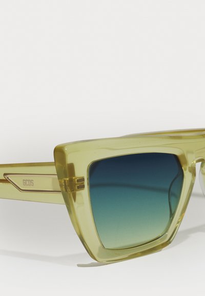 Grün getönte Sonnenbrille mit quadratischem Rahmen. Transparenter, hellgrüner Kunststoff, verlaufende blaue Gläser und eingraviertes Markenlogo an den Bügeln.