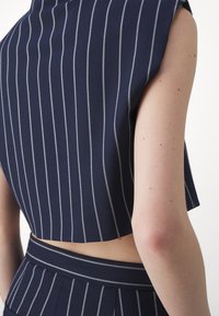 Mörkblå croppad topp med vita ränder, med en strukturerad design och utan ärmar. Slät textur, som framhävs av en horisontell skärning.