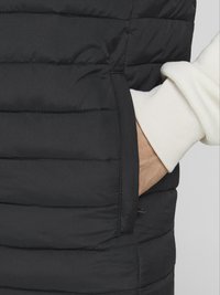Zwarte gewatteerde vest met horizontaal doorstikte secties en zijzak. Bevat een witte ribbelkraag onder de arm van zacht materiaal.