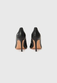 Sorte høye hæler med spiss tå, glatt skinnmateriale, slanke hæler og en lys tan såle. Minimalistisk design uten utsmykninger.