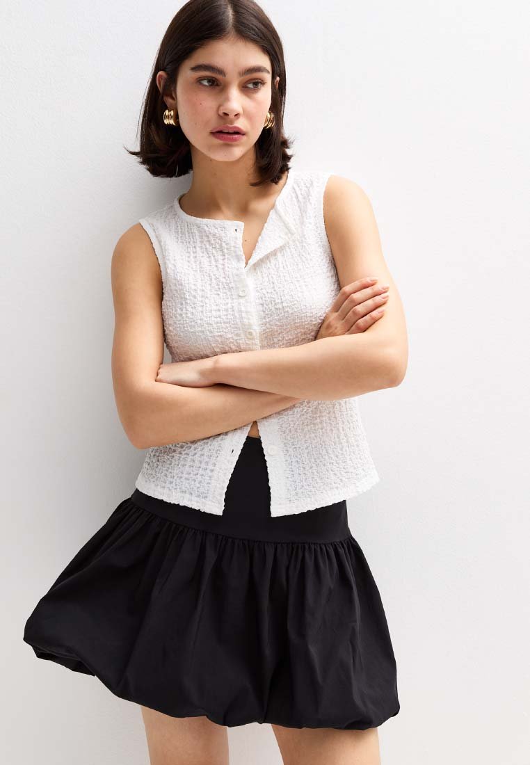 Top senza maniche bianco con una chiusura a bottoni, abbinato a una gonna nera a trapezio. Entrambi i capi hanno uno stile casual e design semplici.