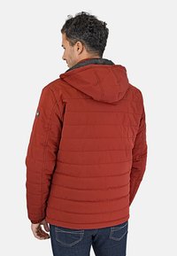 Chaqueta aislante roja con textura acolchada, capucha y detalles en negro. Presenta un logo en el hombro izquierdo y un diseño de dobladillo recto.