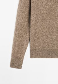 Manica e sezione inferiore del torso di un maglione lavorato a maglia marrone con polsini e orlo a coste su uno sfondo bianco.