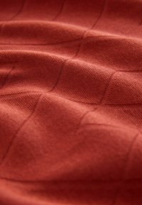 Tissu texturé dans une teinte brun-rouge chaud avec un motif de grille subtil et une texture tissée douce.