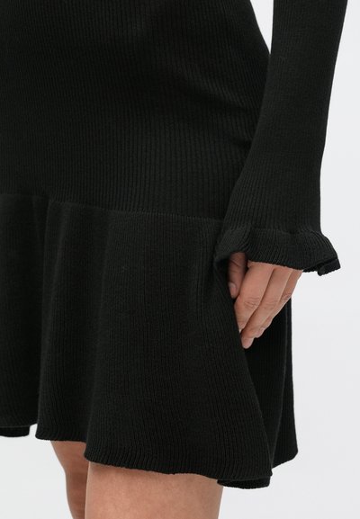 Čierne rebrované úpletové šaty s dlhými rukávmi a rozšíreným lemom, s textúrovaným povrchom a jemnými riasenými detailmi na manžetách.