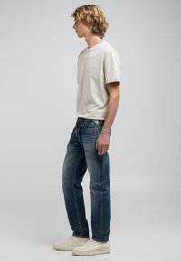 Avslappnad outfit med en krämfärgad t-shirt med kort ärm och mörkblå jeans, kompletterad med vita sneakers, allt med en avslappnad passform.