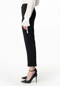 Pantaloni neri in taglio sartoriale con vestibilità slim, caratterizzati da una texture liscia. Abbinati a tacchi a punta neri e una blusa bianca con maniche a volant.