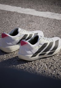 Paar weiße Laufschuhe mit schwarzen Streifen und pinken Fersenlaschen, die auf einer Asphaltfläche liegen.
