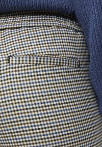Pantalons à carreaux avec un motif bleu, marron et blanc, dotés d'une taille en tricot bleu contrastant. Comprend une poche arrière.