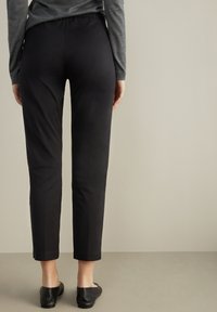 Svarta, figurnära byxor med elastisk midja, kort längd, slät textur och enkel konstruktion. Bärs med svarta platta skor.