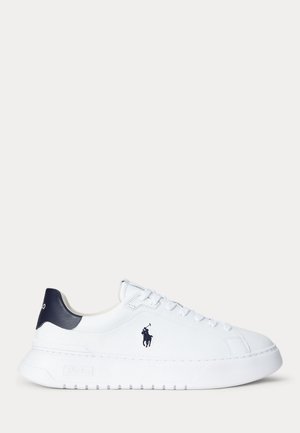 Witte lage sneaker met marineblauwe hielkap, veters aan de voorkant en zwarte polo-speler logo aan de zijkant.