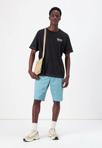 Black cotton t-shirt, light blue shorts, beige crossbody bag, and tan sneakers with white socks. Simple, casual outfit on a model.