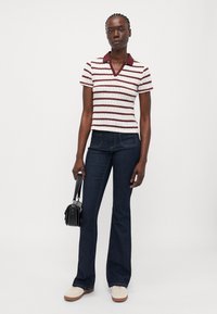 Stripet strikket polo skjorte med en mørkerød krage, tilpasset passform; parret med mørkeblå utflarede jeans og lyse sneakers. Liten håndveske holdes.