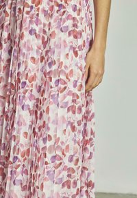 Vestido plisado con un estampado floral en tonos de rosa, púrpura y rojo sobre un fondo claro; la tela parece ligera y texturizada.