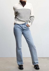 Maglione bianco a righe con colletto a mezza zip, abbinato a jeans azzurri chiari e mocassini neri. Il maglione ha una texture a coste, i jeans sono a gamba dritta.