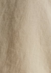 Gros plan d'un tissu beige tissé montrant une texture détaillée et de petits motifs de tissage irréguliers.