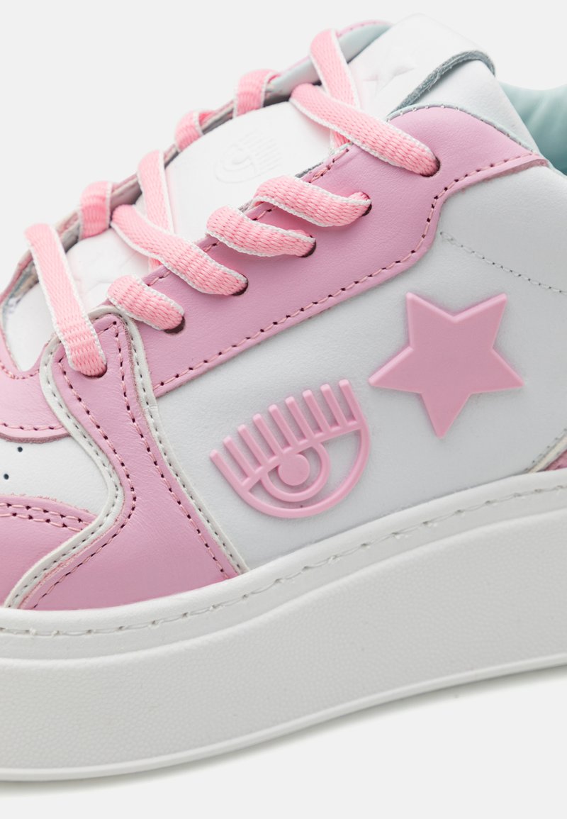 Weiße Ledersneaker mit pinken Akzenten, die ein strukturiertes Design, Sterne- und Augenmotive sowie pinke Schnürsenkel auf einer dicken weißen Sohle aufweisen.
