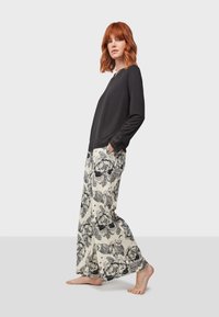 Haut noir à manches longues avec des accents en dentelle, associé à un pantalon crème ample avec un motif floral noir et de hiboux.