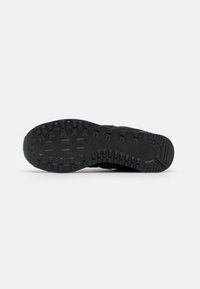 Schwarze Gummisohle eines Sneakers mit einem strukturierten Profil, das verschiedene Rillen und Erhöhungen aufweist, um den Grip und die Traktion zu verbessern.