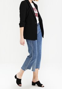 Svart skräddarsydd kavaj över en vit grafisk t-shirt, kombinerad med avkortade blå jeans och svarta öppna blockklackar.