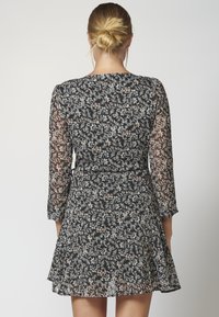 Schwarzes Blumenkleid mit langen, durchsichtigen Ärmeln, tailliertem Schnitt und ausgestelltem Rock, ausgestattet mit einem Muster aus kleinen Blumen in sanften Farben.