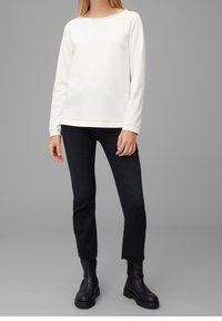Maglietta bianca a maniche lunghe con scollo ampio, abbinata a jeans neri cropped con orlo sfilacciato e robusti stivali neri alla caviglia.