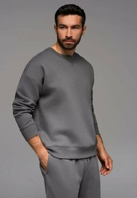 Grauer Hoodie aus einem weichen, strukturierten Material mit Rundhalsausschnitt und gerippten Bündchen, kombiniert mit passenden grauen Hosen.