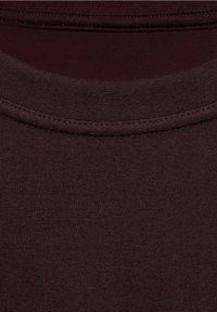 Vue en gros plan d’un tissu tricoté marron foncé montrant l’encolure ronde et les détails des coutures d’un vêtement.