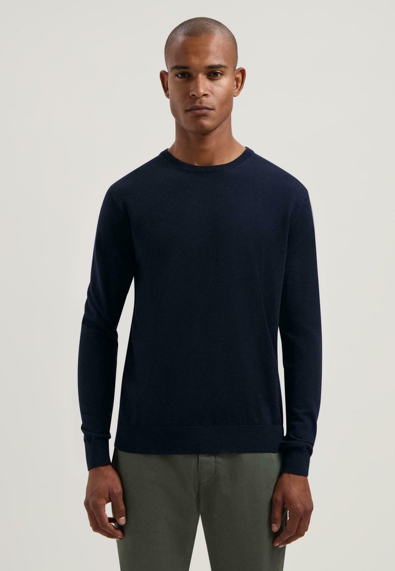 Maglione lavorato a maglia blu navy con collo rotondo, maniche lunghe e polsini e orlo a coste. Texture liscia, design semplice senza motivi o dettagli decorativi.