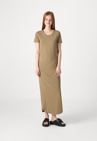 Robe maxi olive, à manches courtes, ajustée, en tissu doux, avec un décolleté rond et une silhouette droite. Portée avec des sandales noires à enfiler.