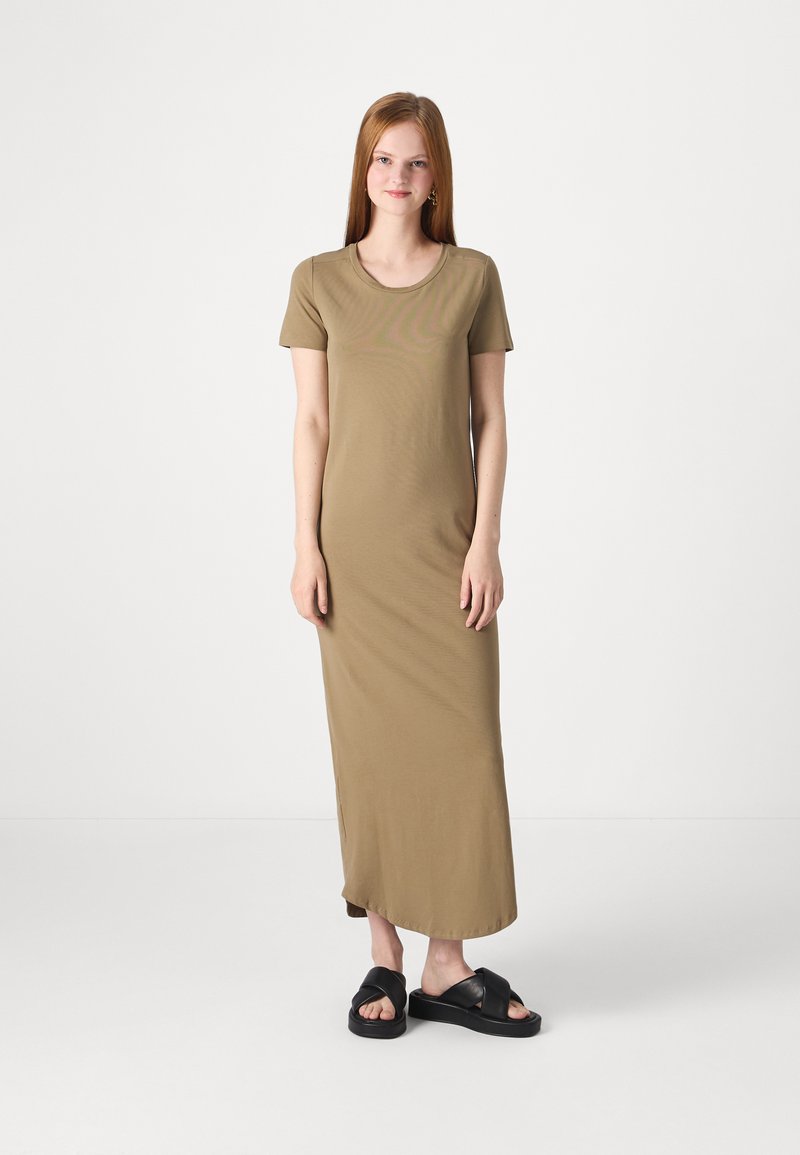 Robe maxi olive, à manches courtes, ajustée, en tissu doux, avec un décolleté rond et une silhouette droite. Portée avec des sandales noires à enfiler.