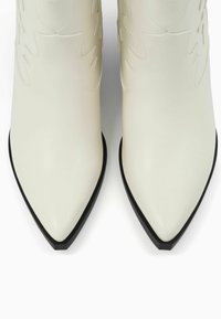 Białe skórzane botki sięgające kostki z szpiczastym noskiem, z delikatnym tłoczonym wzorem i kontrastującą czarną podeszwą. Gładka faktura z eleganckim designem.