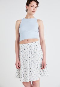 Lyseblå ribbet crop top med rund halslinning, kombinert med et flytende hvitt skjørt med små blå blomsterprint. Elastisk midjebånd synlig.