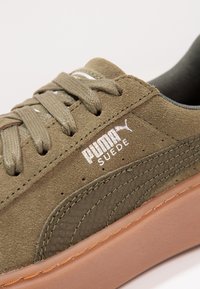 Olivově zelené semišové tenisky s texturovanými akcenty, s tónovou nití, gumovou podrážkou a bílým logem Puma na boku.