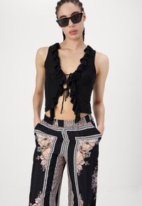 Fekete, ujjatlan felső fodros elejével és megkötős részletével, laza, fekete és mintás, virágmotívumos bővülő nadrággal párosítva.