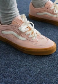 Sneakers in suede rosa chiaro con dettagli bianchi, caratterizzati da una punta rotonda, chiusura con lacci e suola in gomma texture. Indossati con calzini grigi a costine.