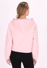 Lichtroze cropped hoodie van zachte stof, met een grote capuchon, elastische manchetten en een relaxed fit, van achteren getoond.