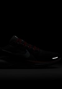 Chaussure de sport noire avec des lacets rouges, tige en maille et accents réfléchissants. Comprend une semelle texturée et un logo Nike bien en vue.