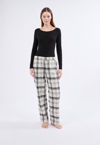 Un body de manga larga negro combinado con pantalones de pijama de cuadros color crema que presentan líneas negras y grises. Los pantalones tienen una cintura con cordón ajustable.