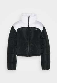 Giacca a vento nera e bianca con collo alto, design accorciato e zip frontale. Presenta il logo sul lato sinistro del petto e polsini a coste.