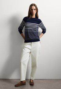 Maglione a righe blu navy con righe bianche, scollo rotondo, maniche lunghe; abbinato a pantaloni bianchi e scarpe in suede marroni. Texture liscia.
