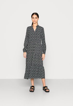 Vestido preto floral com gola, mangas longas e bainha em camadas. Combinado com sandálias altas pretas. Tecido suave com um brilho sutil.